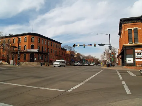 Main Street at 3rd Avenue in downtown Longmont on a late-winter day, the 1881 Dickens Opera House on the right corner and a three-storey red-brick block across the street, looking north up the 300 block under bare trees.