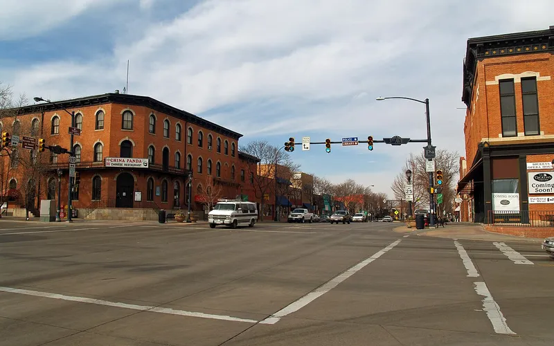 Main Street at 3rd Avenue in downtown Longmont on a late-winter day, the 1881 Dickens Opera House on the right corner and a three-storey red-brick block across the street, looking north up the 300 block under bare trees.