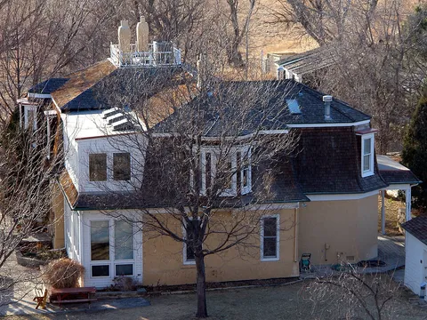 The historic Sandstone Ranch house, now the park's visitor center, a two-storey farmhouse with a mansard roof and white dormers, seen from above through bare trees on a February afternoon.